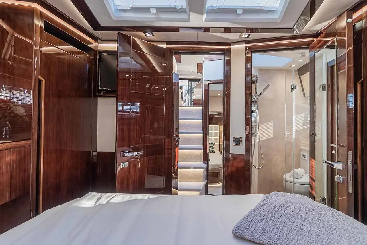 Luxurious yacht interior showing a bedroom, elegant wooden panels, doors, a staircase, and a glimpse of a bathroom.