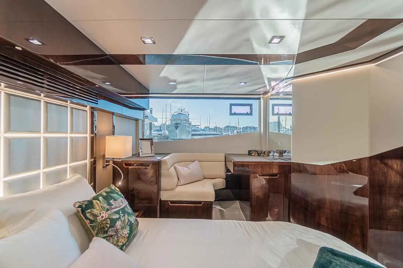Luxurious yacht interior featuring a queen bed, sleek furniture, a small seating area, and large windows overlooking a marina.