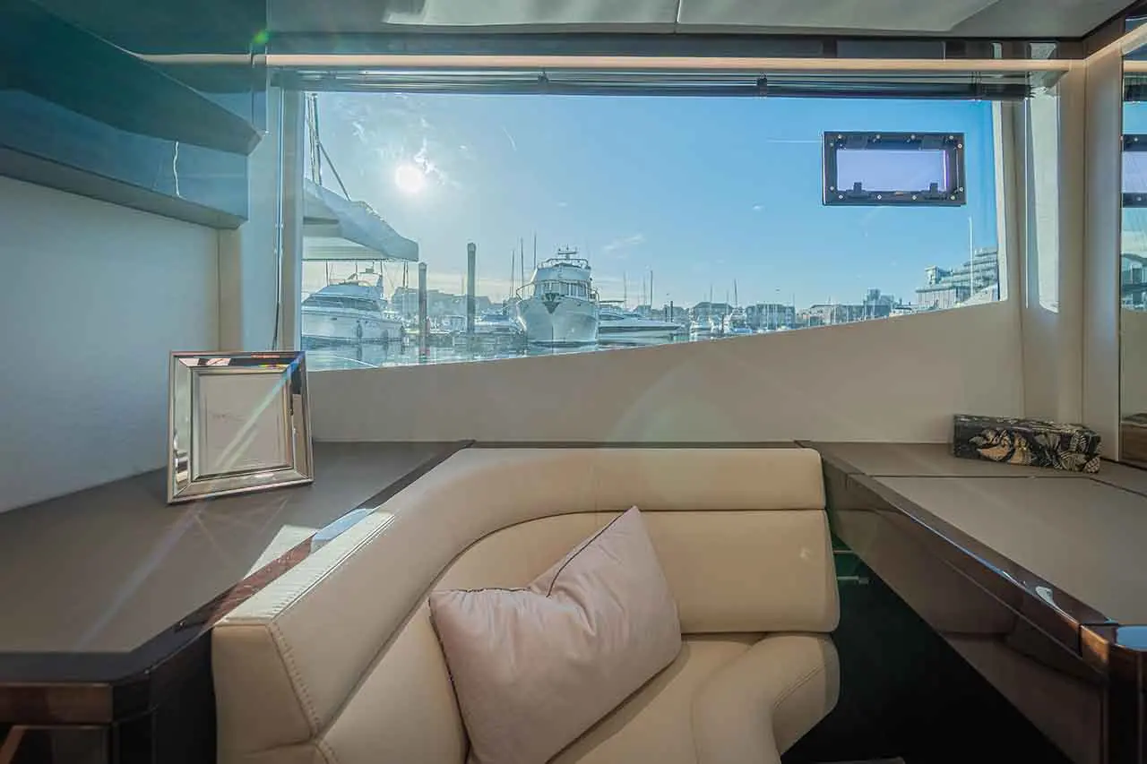 Luxury yacht interior with cream leather sofa, cushions and marina views through panoramic windows.