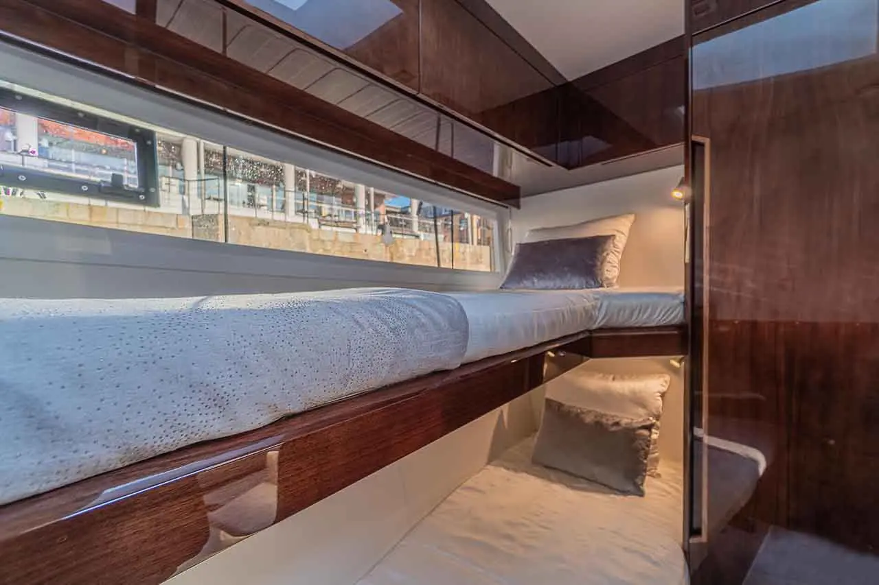 Interior view of a modern boat cabin featuring a sleek bed, cushions, and a window with light streaming in.