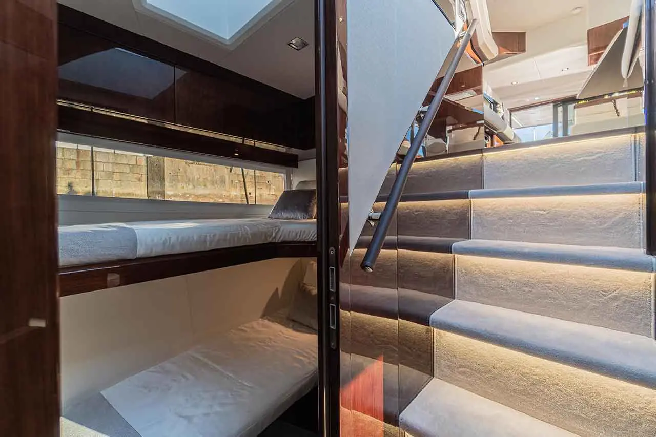 Interior view of a boat showing a bunk bed area and illuminated staircase leading up to a cabin with modern furnishings.