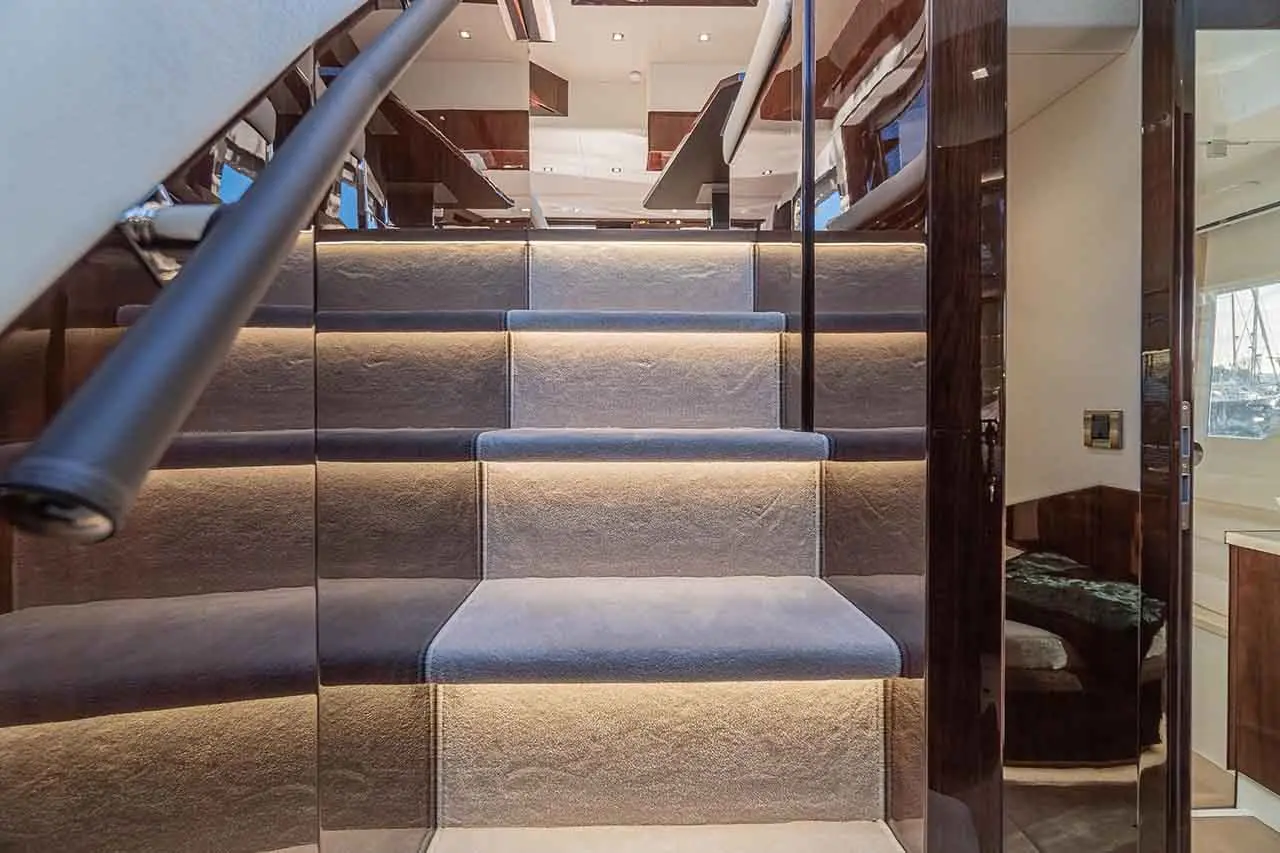 Interior view of a luxury yacht staircase, featuring illuminated steps, glass panels, and modern decor.