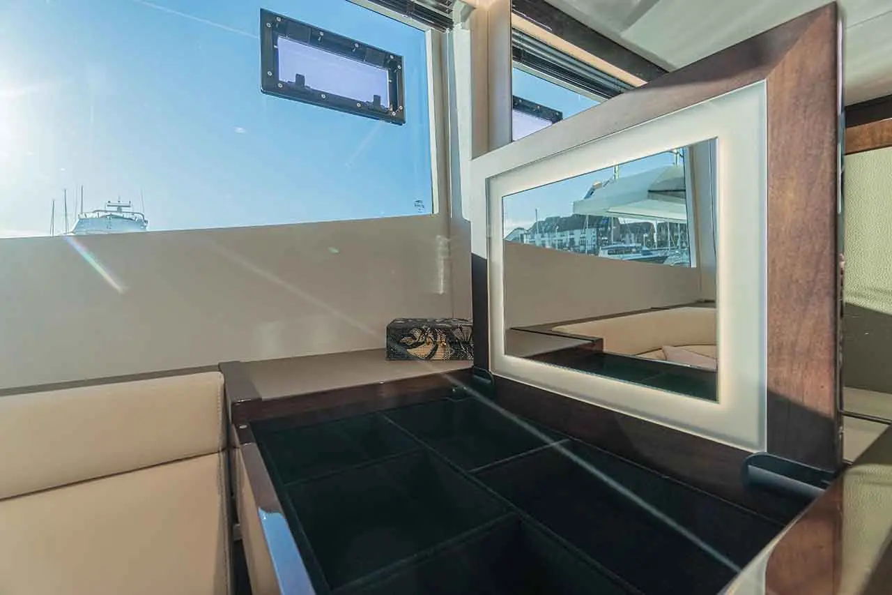 Interior of a yacht featuring a mirrored cabinet, sunlight streaming in through windows, with a decorative box on the table.