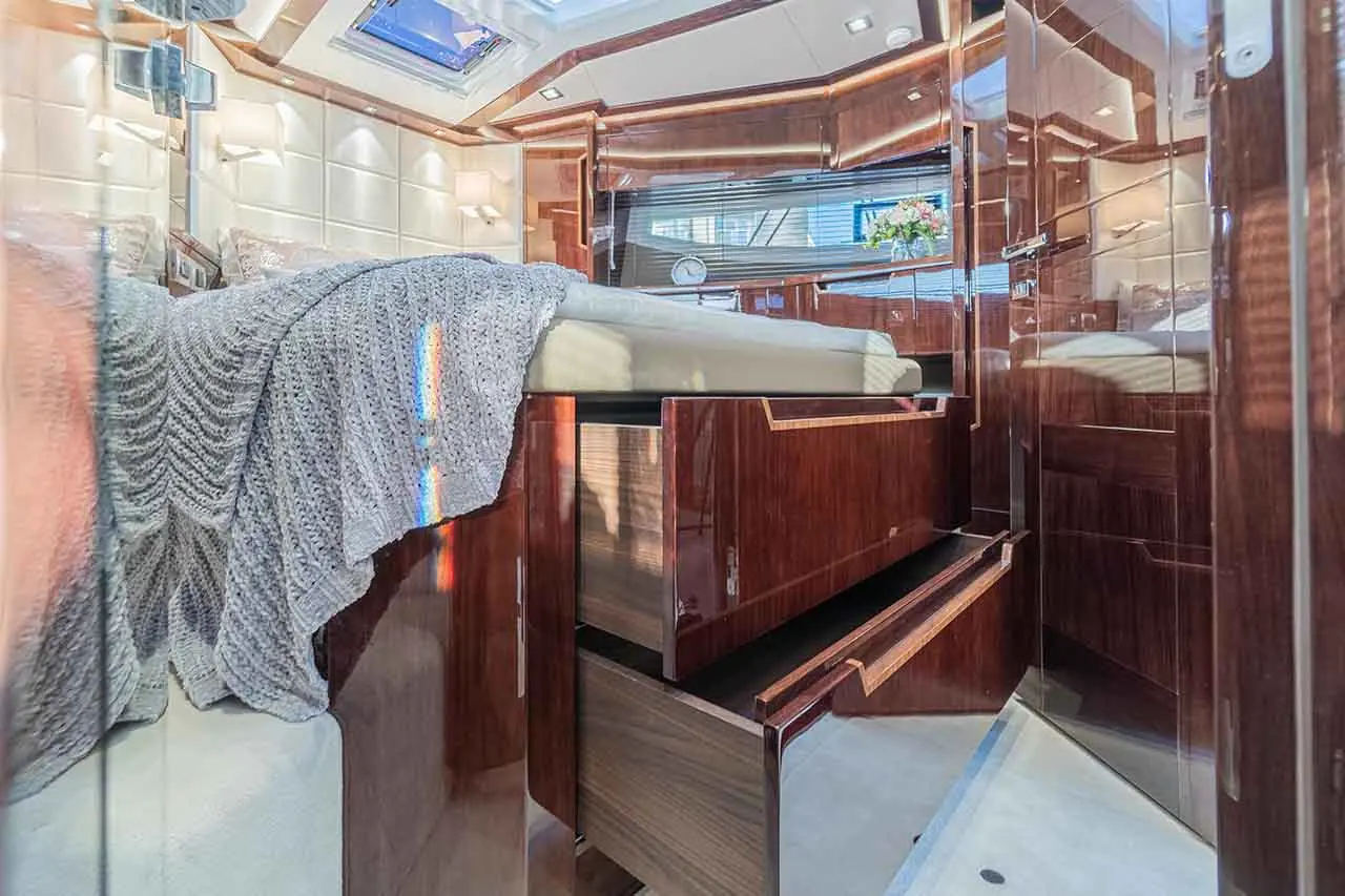 Luxurious boat cabin with a double bed, elegant wooden storage drawers, and natural light streaming through a skylight.