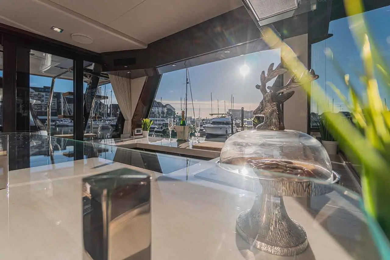 Luxury yacht interior with modern décor, marina view, and a decorative reindeer figurine atop a glass cake stand.