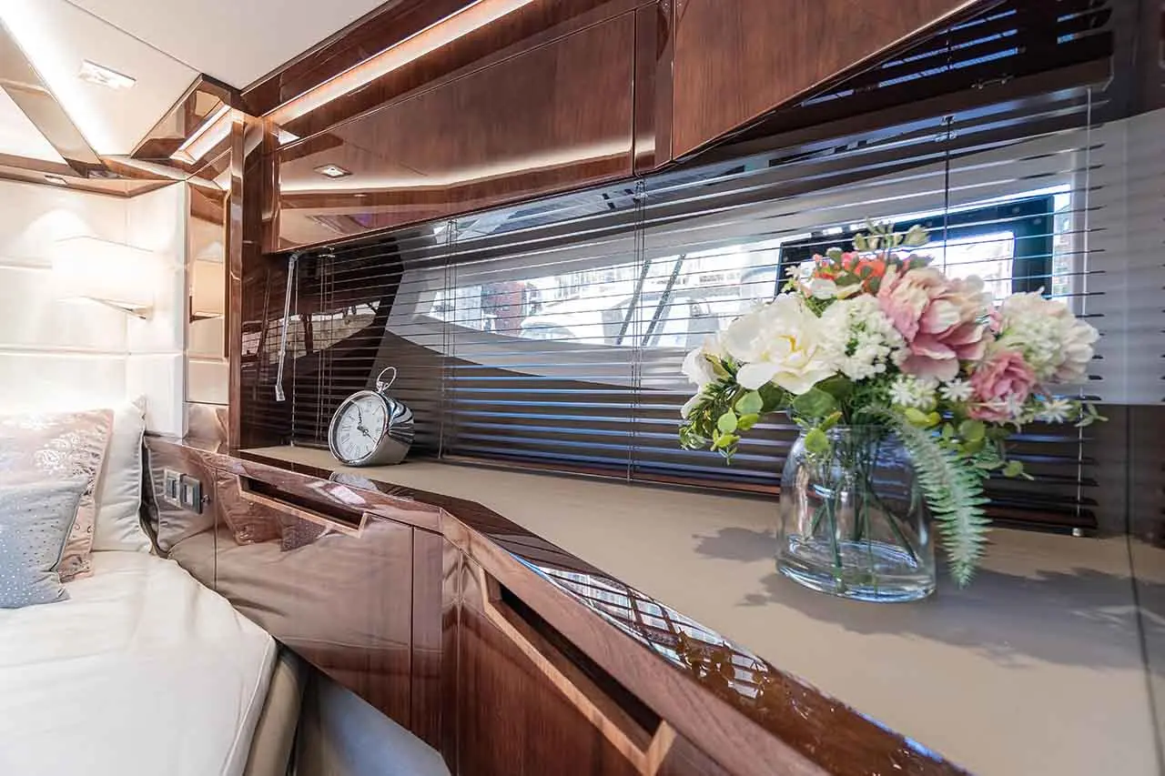 Luxurious interior view featuring a clock and a vase of flowers on a sleek wooden surface with natural light filtering through blinds.