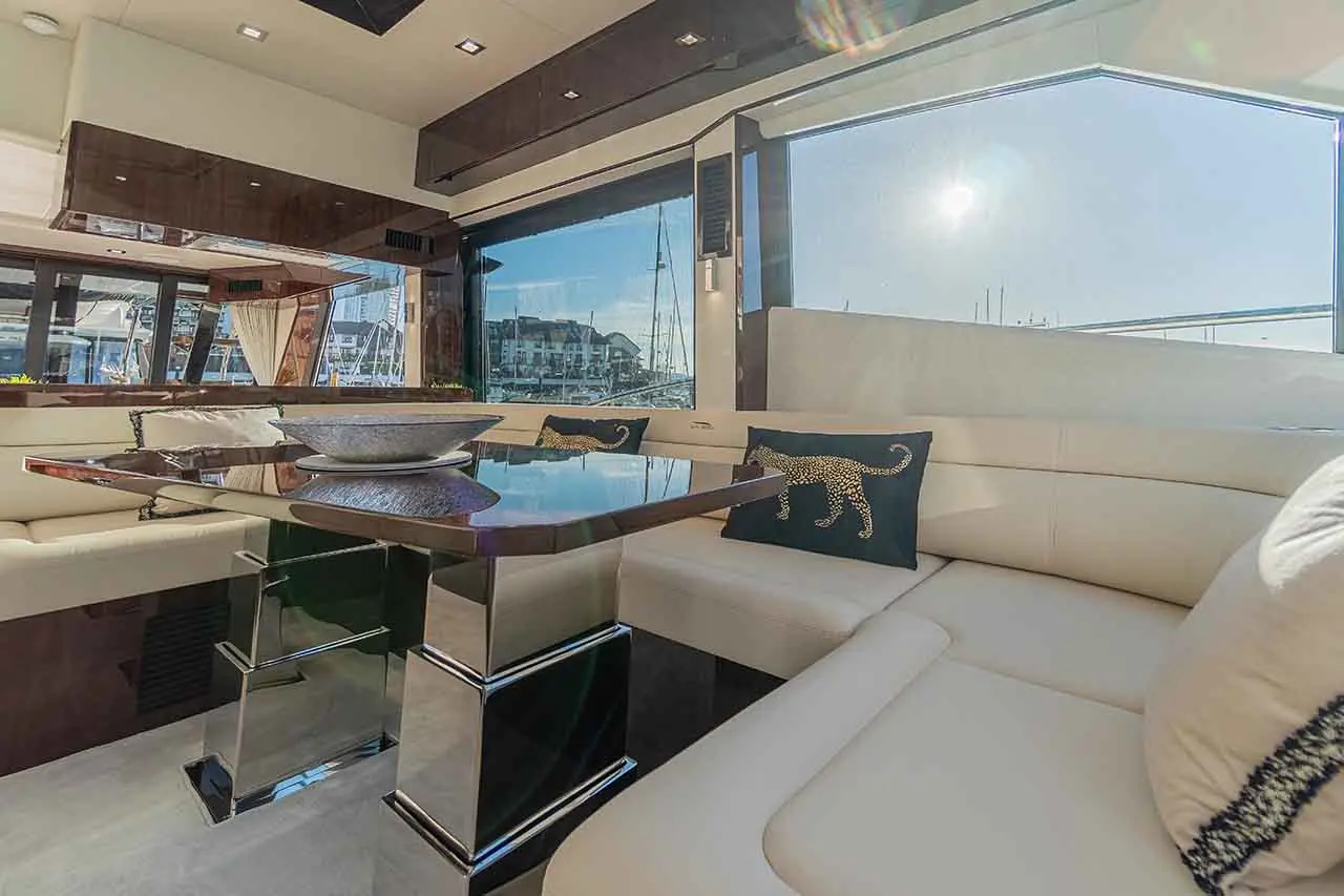 Luxurious yacht interior with a modern table, plush seating, and view of the marina through large windows. Sunlight visible.