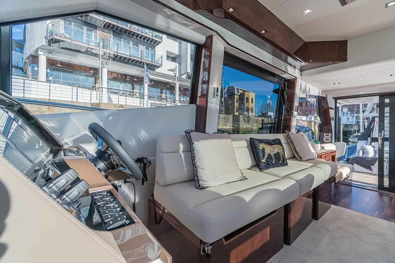 Luxury yacht interior featuring a steering wheel, cream leather seating, and a leopard print cushion with views of the marina.