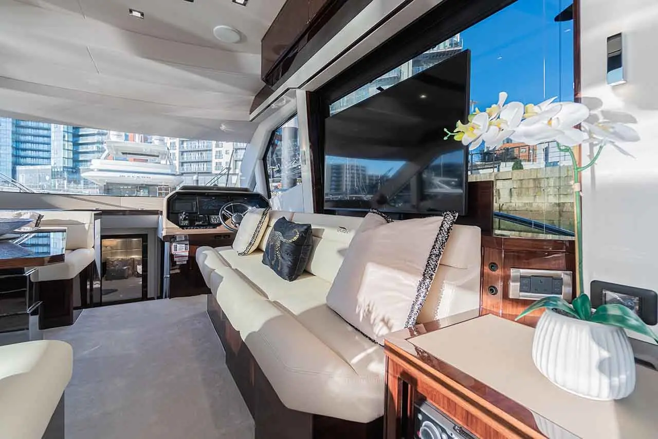 Interior of a luxury yacht showcasing cream-coloured seating, large windows, a TV, and a decorative orchid plant.