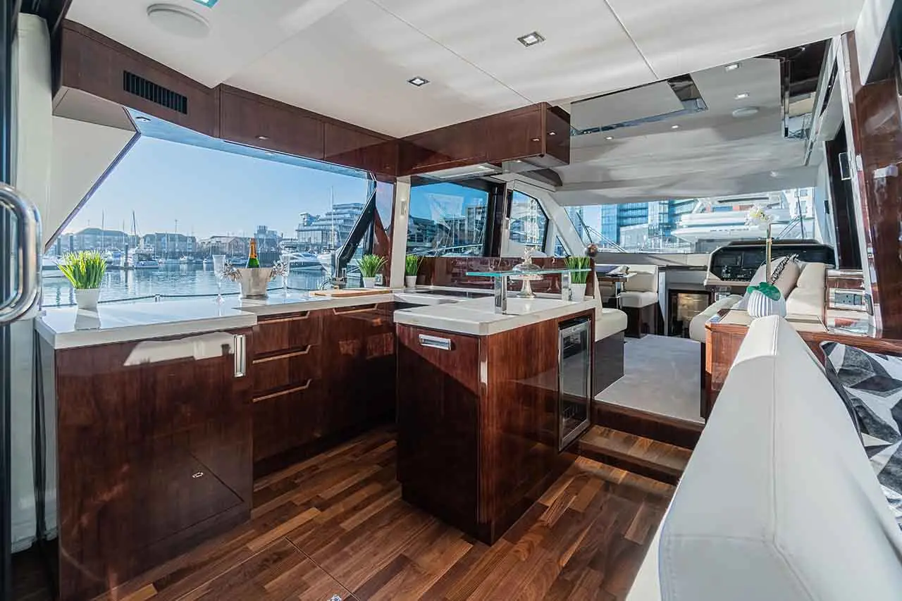 Luxurious yacht interior featuring a modern kitchen, large windows, and a scenic marina view, with potted plants and elegant decor.