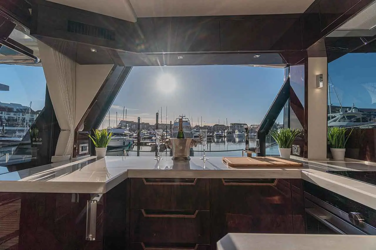 Luxury yacht galley featuring a view of a marina, with a silver champagne bucket, glasses, and potted plant on the countertop.