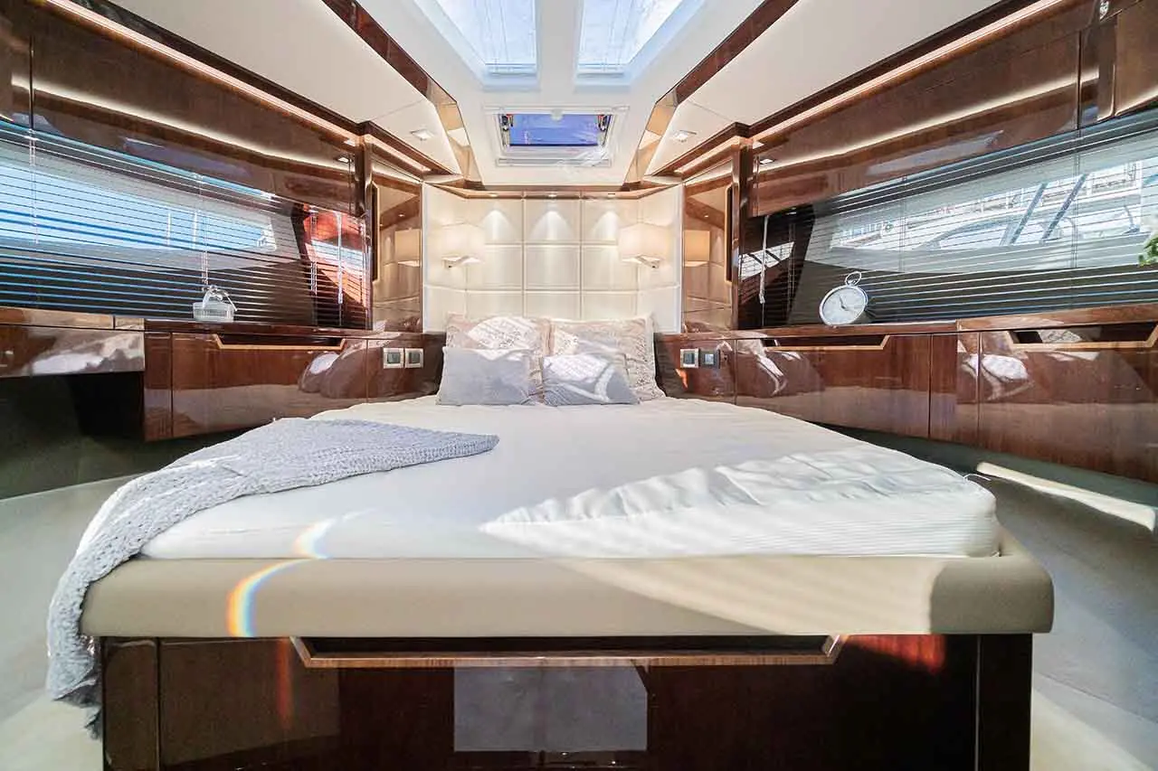 Luxurious yacht bedroom with a double bed, wooden cabinetry, and natural light from skylights. Decorative cushions and clock visible.