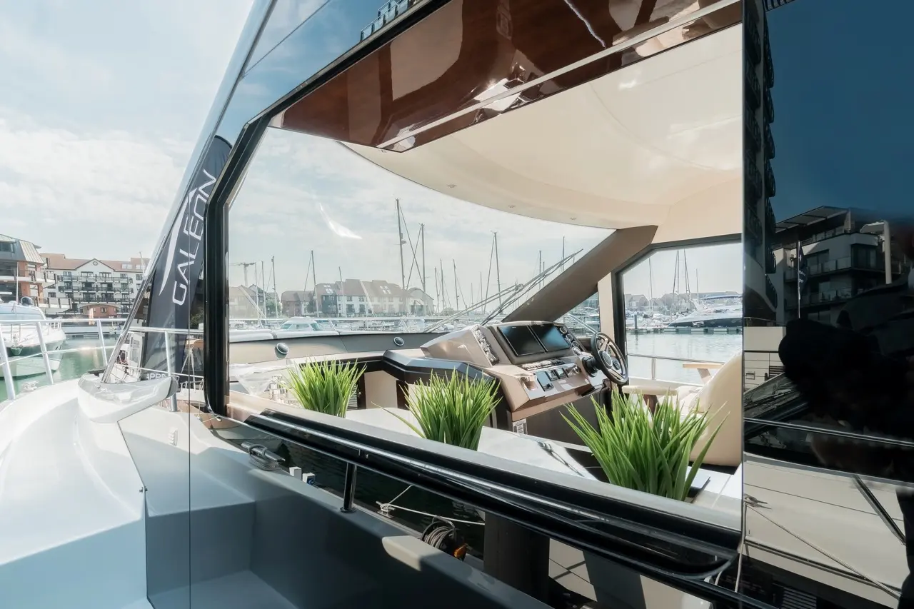 Modern yacht interior featuring a control panel, steering wheel, and decorative plants with a marina view.