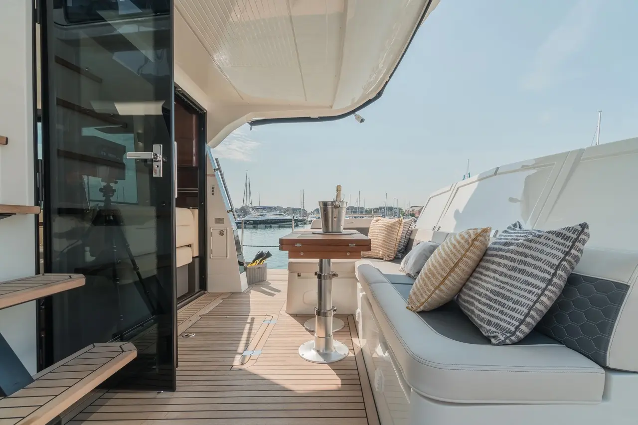 Luxurious yacht deck with plush cushions, a table, and a view of the marina and boats on a sunny day.