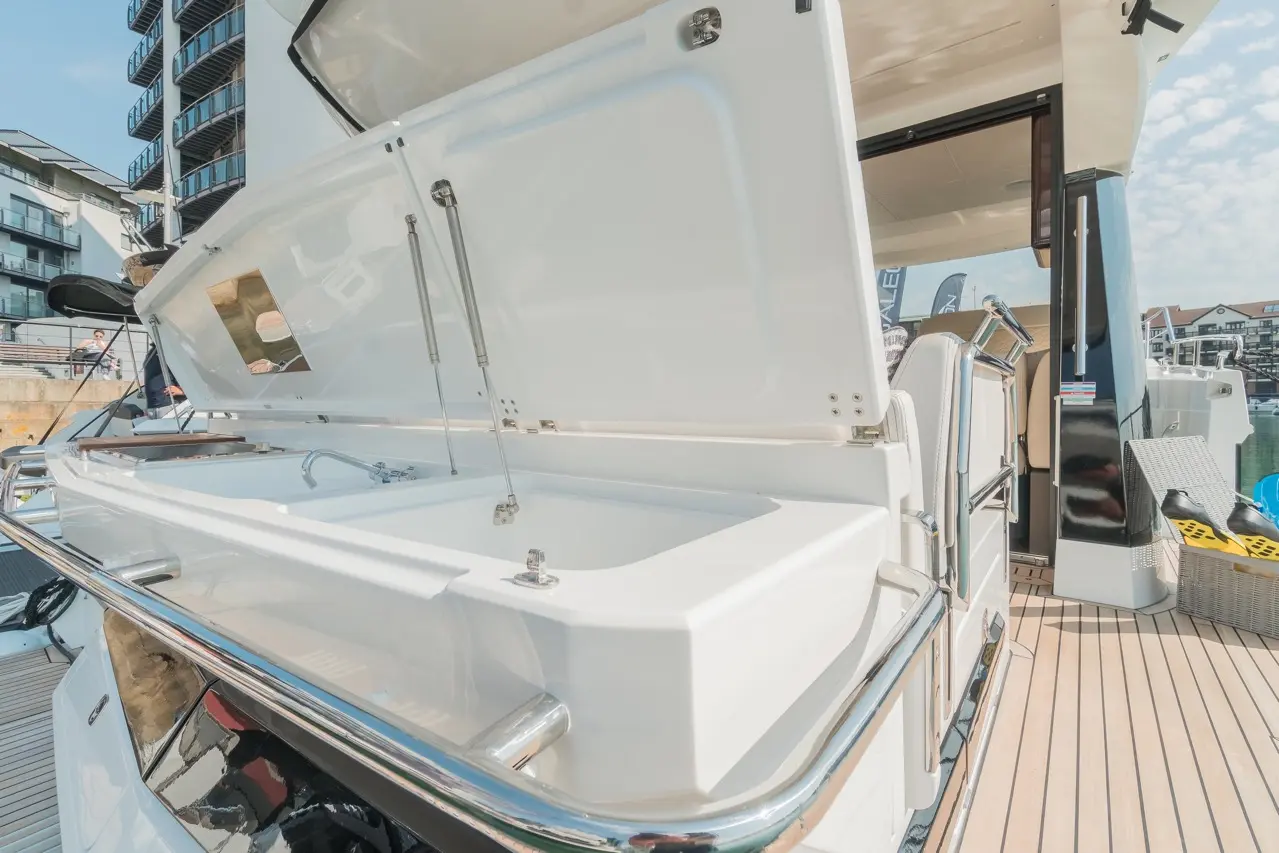 A bright, modern boat deck featuring a white open storage compartment with stainless steel fittings and nearby seating.