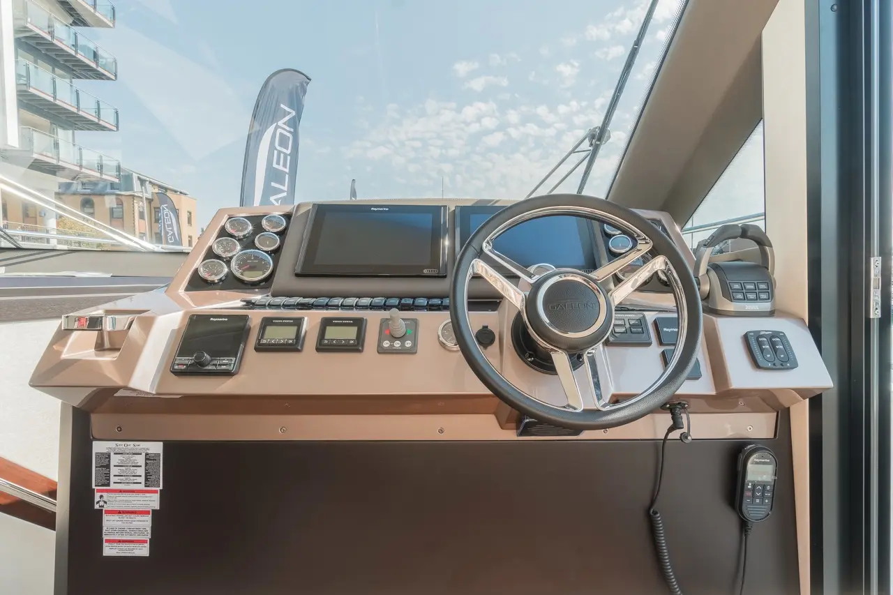 Stylish yacht control panel featuring a steering wheel, gauges, and a display screen, with nearby buttons and a radio.