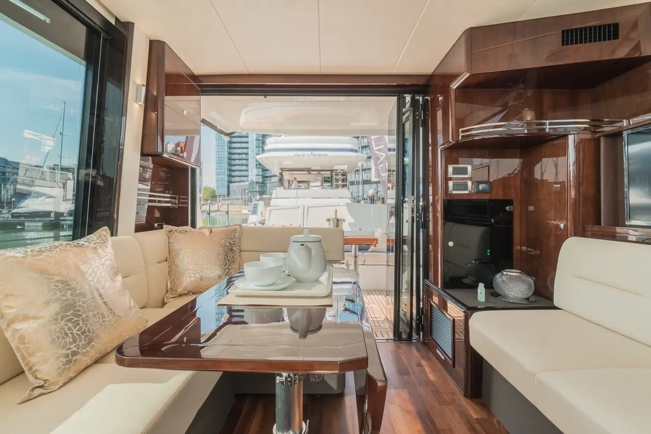 Modern yacht interior featuring a dining area, plush cushions, and large glass doors opening to the waterfront view.