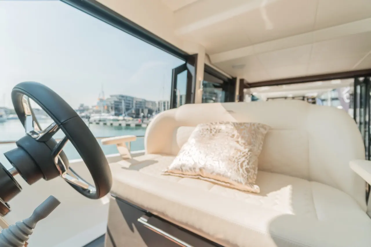Luxury yacht interior featuring a plush seat with a decorative pillow and a steering wheel, overlooking a marina.