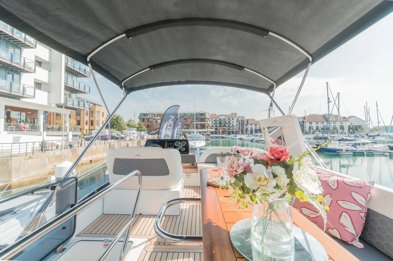 Interior of a luxury yacht showing wooden table, flowers in a vase, marina view, and buildings under a clear sky.