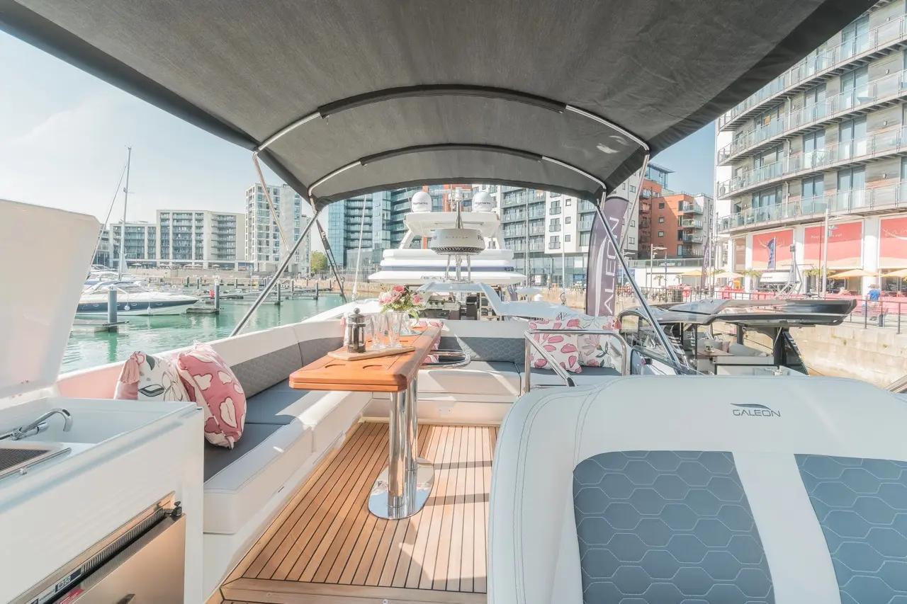 Luxurious yacht interior featuring a dining area, plush cushions, and scenic marina views with modern buildings in the background.