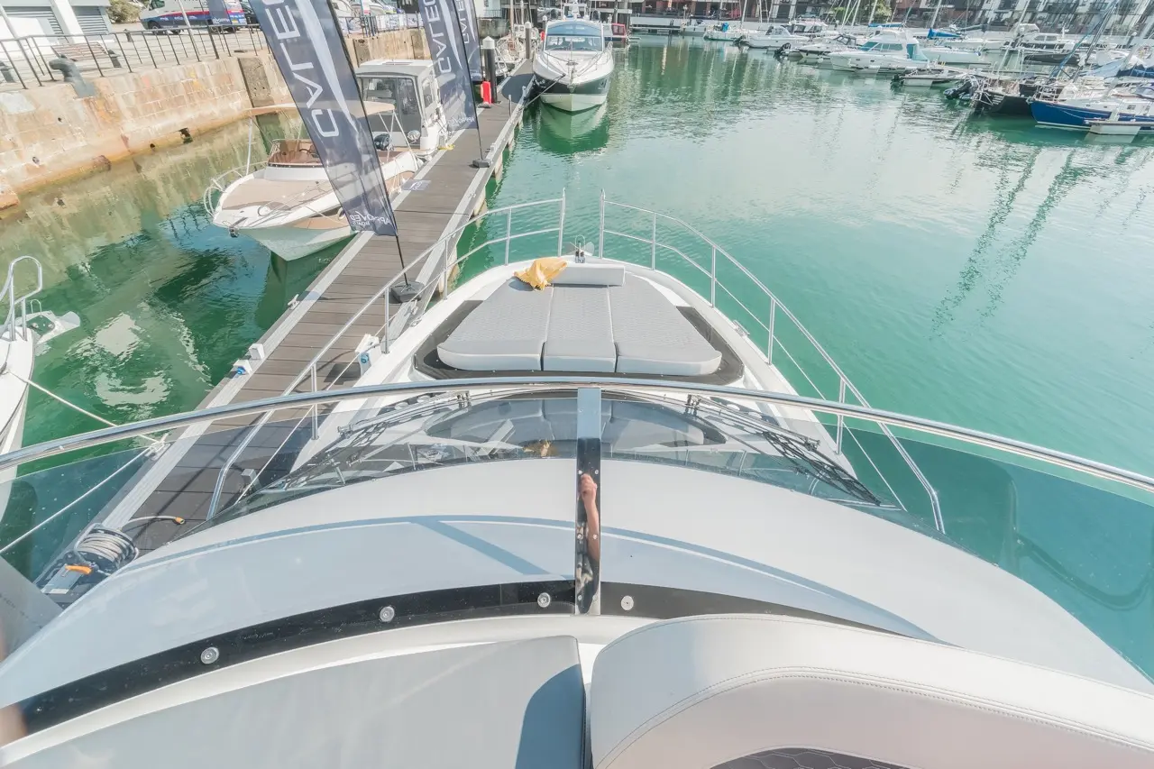 View from the bow of a luxury yacht, with boats docked and reflections on the green water in a marina.