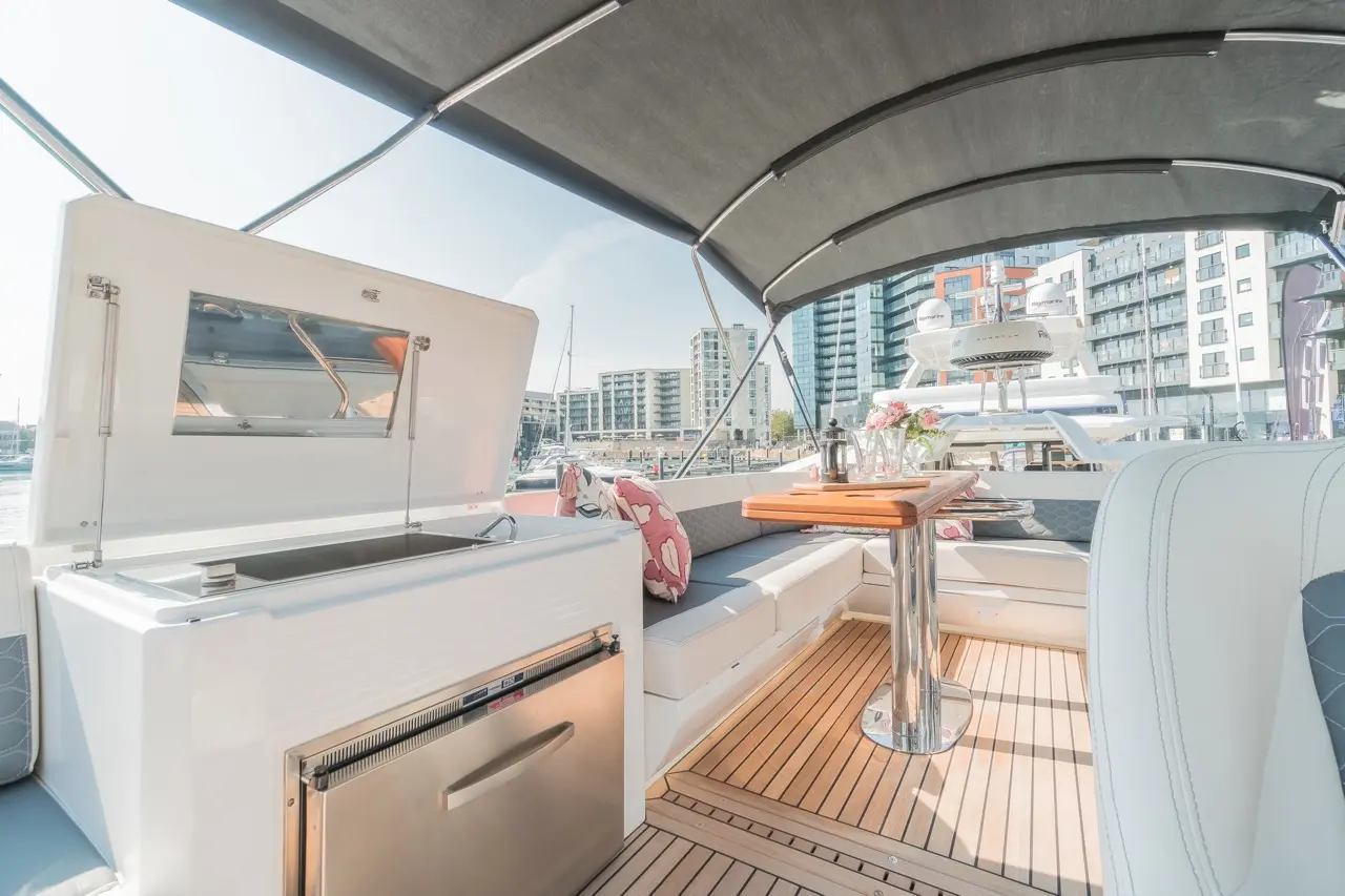 Luxury yacht interior featuring a sleek kitchenette, dining area, and modern decor, overlooking a marina with buildings in background.