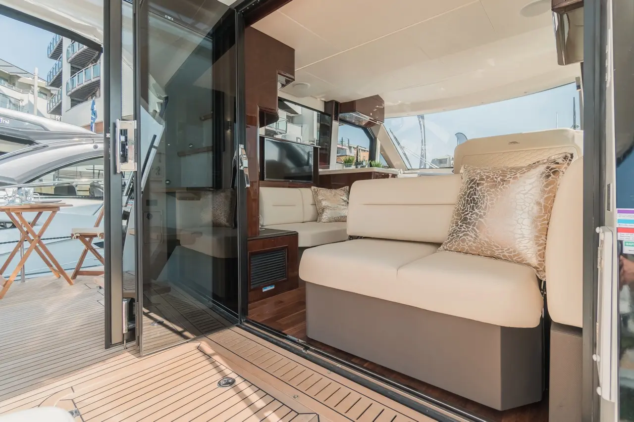 Luxurious yacht interior with plush seating, large glass doors, and stylish decor, overlooking a marina with boats.