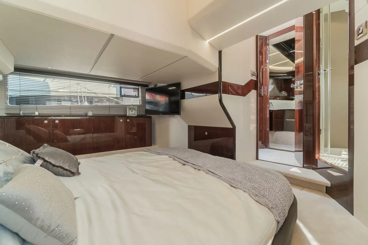 Luxury yacht bedroom featuring a double bed, wooden cabinetry, a TV, and a door leading to an en-suite bathroom.