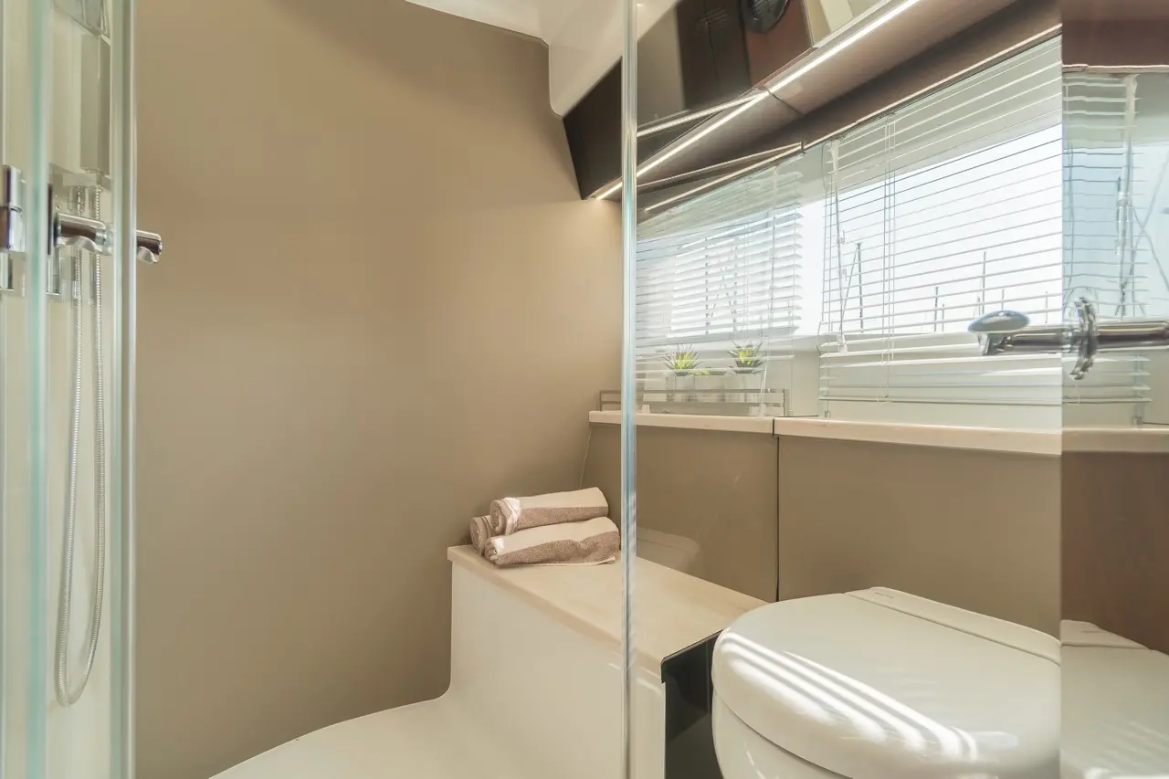 Modern bathroom with a shower, stylish beige walls, towels stacked on a ledge, and a bright window with small plants.