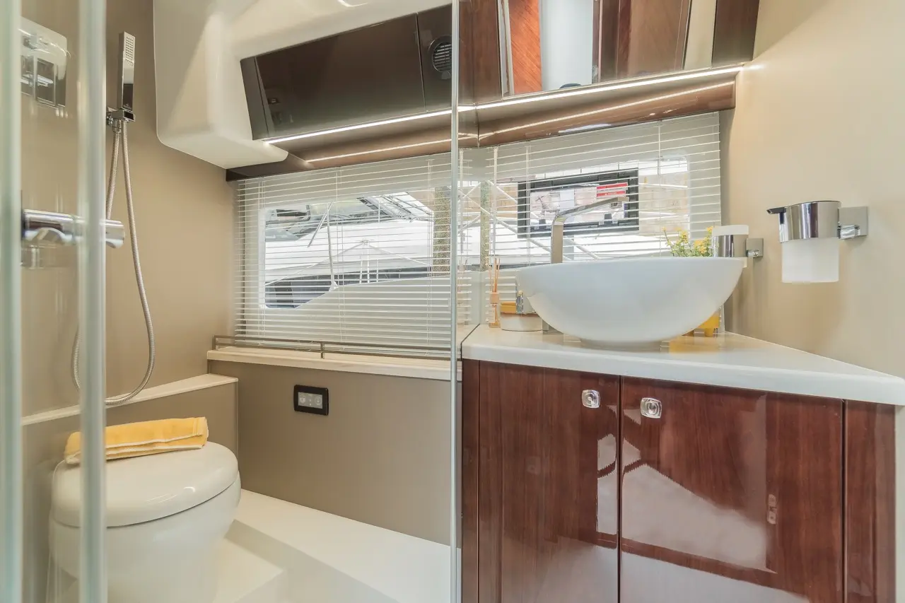 Modern bathroom featuring a shower, toilet, and a stylish sink with natural light through blinds. Yellow towel on the ledge.