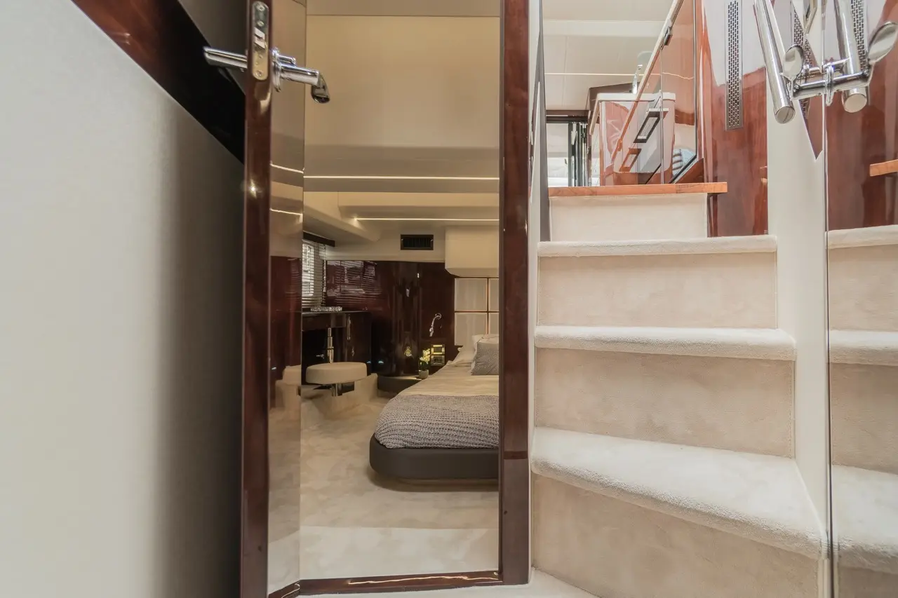 View of a stylish cabin interior with a bed, mirrored door, and cream carpeted stairs leading to a second level.