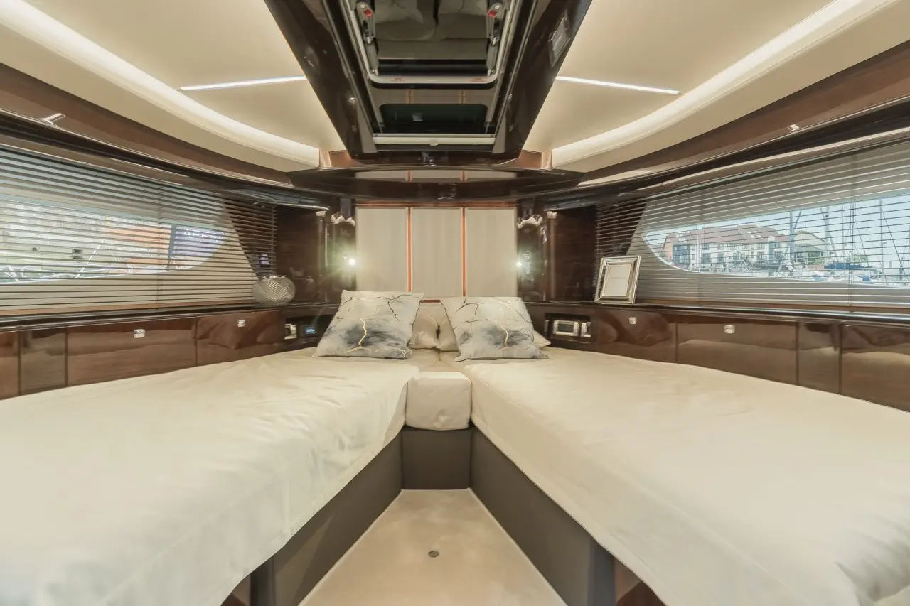 Luxurious yacht interior showcasing two single beds, decorative pillows, and soft lighting with marina views through blinds.