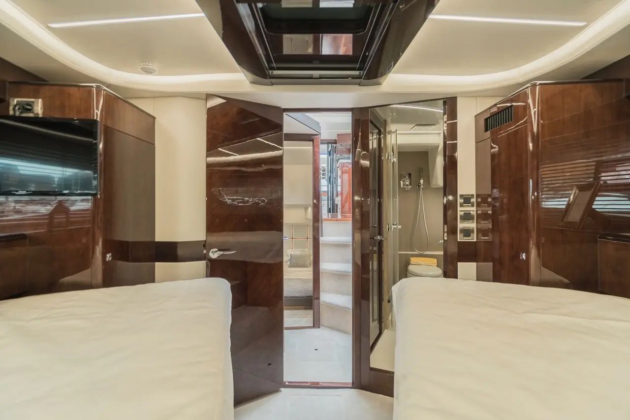 Luxurious yacht interior featuring two single beds, wood finishes, and an en-suite bathroom with shower and toilet.