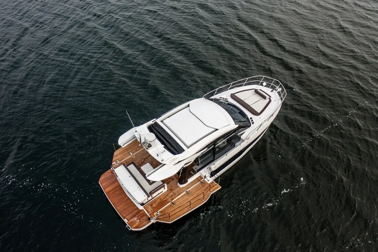 Sleek luxury yacht with wooden deck floating on calm water, showcasing modern design and spacious lounge area on top.
