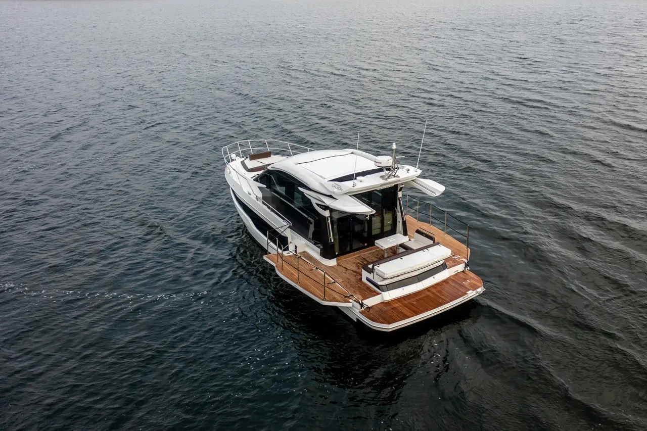 Luxury motorboat with a wooden deck floating on calm water, featuring a covered dining area and sleek modern design.