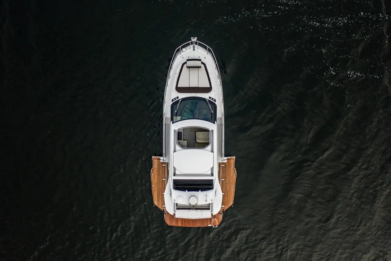 Aerial view of a sleek white yacht with wooden decking, floating on dark water, showcasing luxury boating design.