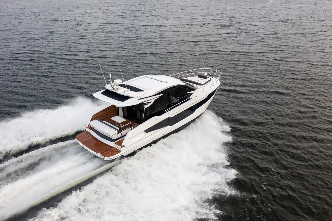 A modern motor yacht gliding over dark water, creating a white wake, showcasing a sleek design and wooden deck.