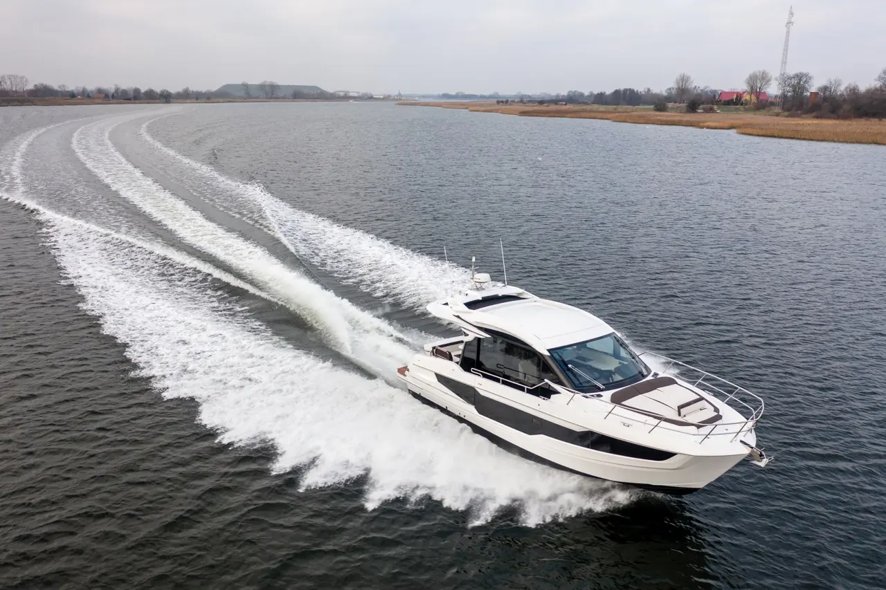 A sleek boat speeds across a calm waterway, creating white wake trails against a cloudy sky, showcasing leisure boating.