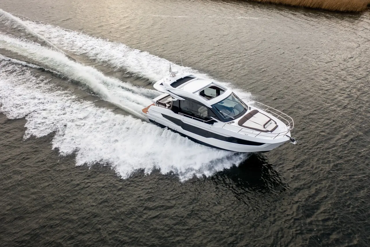 A sleek white motorboat glides across water, leaving a trail of foamy waves in its wake under a cloudy sky.