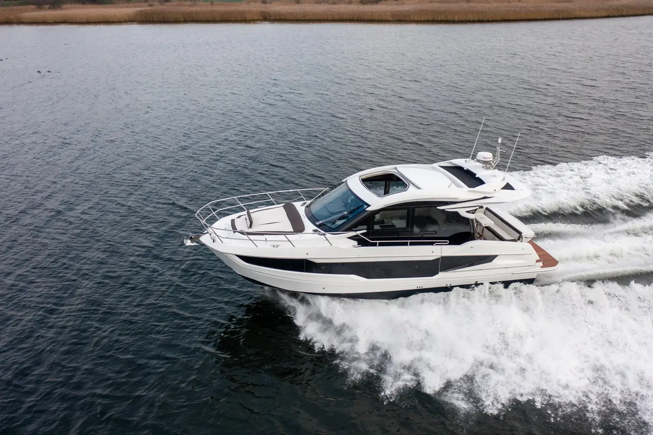 A sleek white motorboat accelerates over rippling water, leaving a frothy wake behind it in a calm, scenic environment.