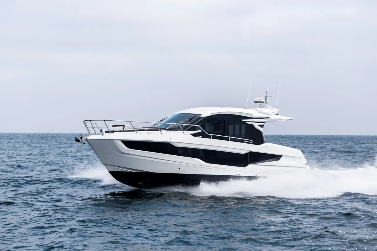 A sleek white motor yacht glides through the ocean waves under a cloudy sky, showcasing its modern design.
