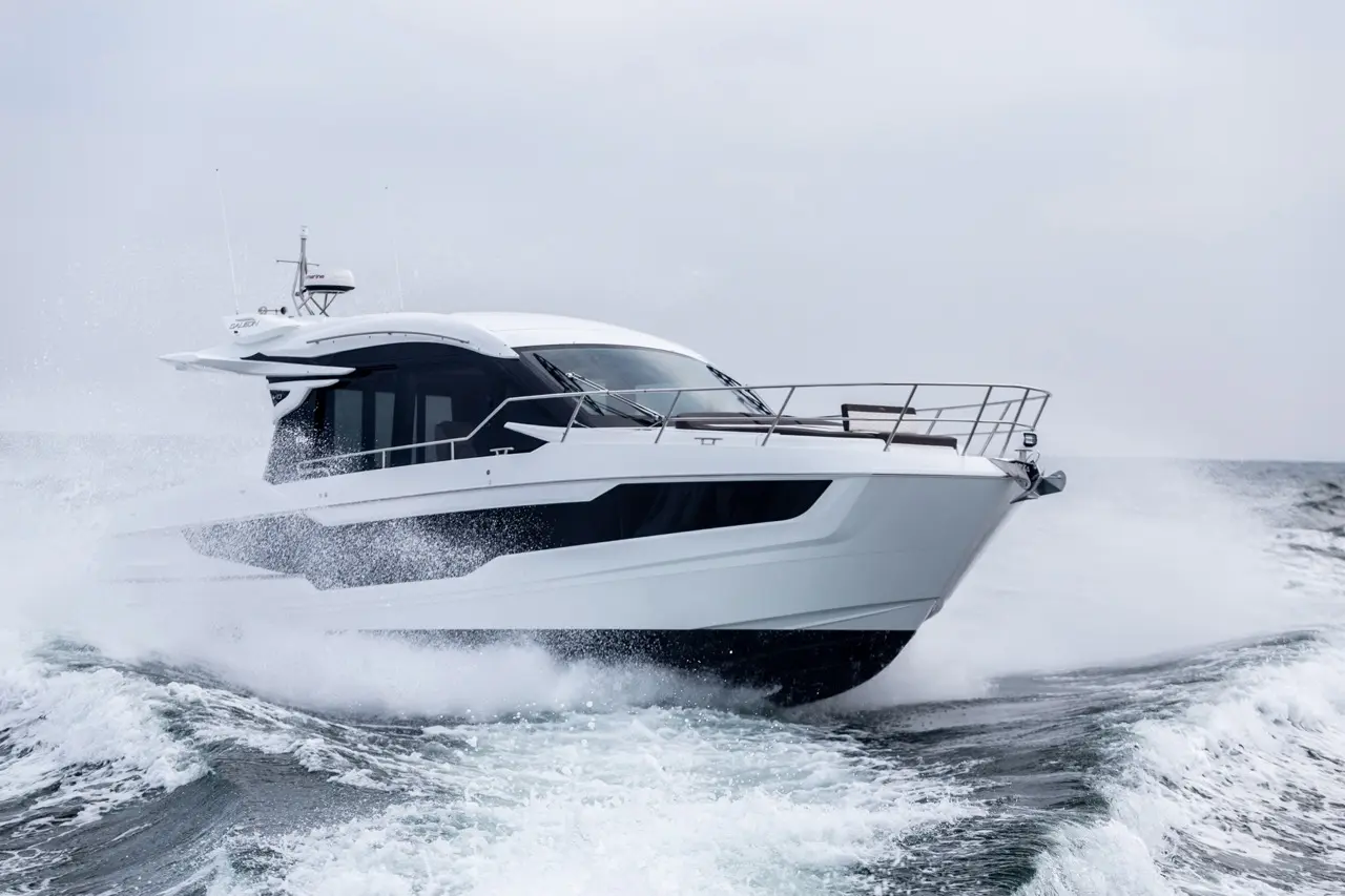 A sleek white yacht splashes through waves at high speed, showcasing luxury design against a cloudy sky.