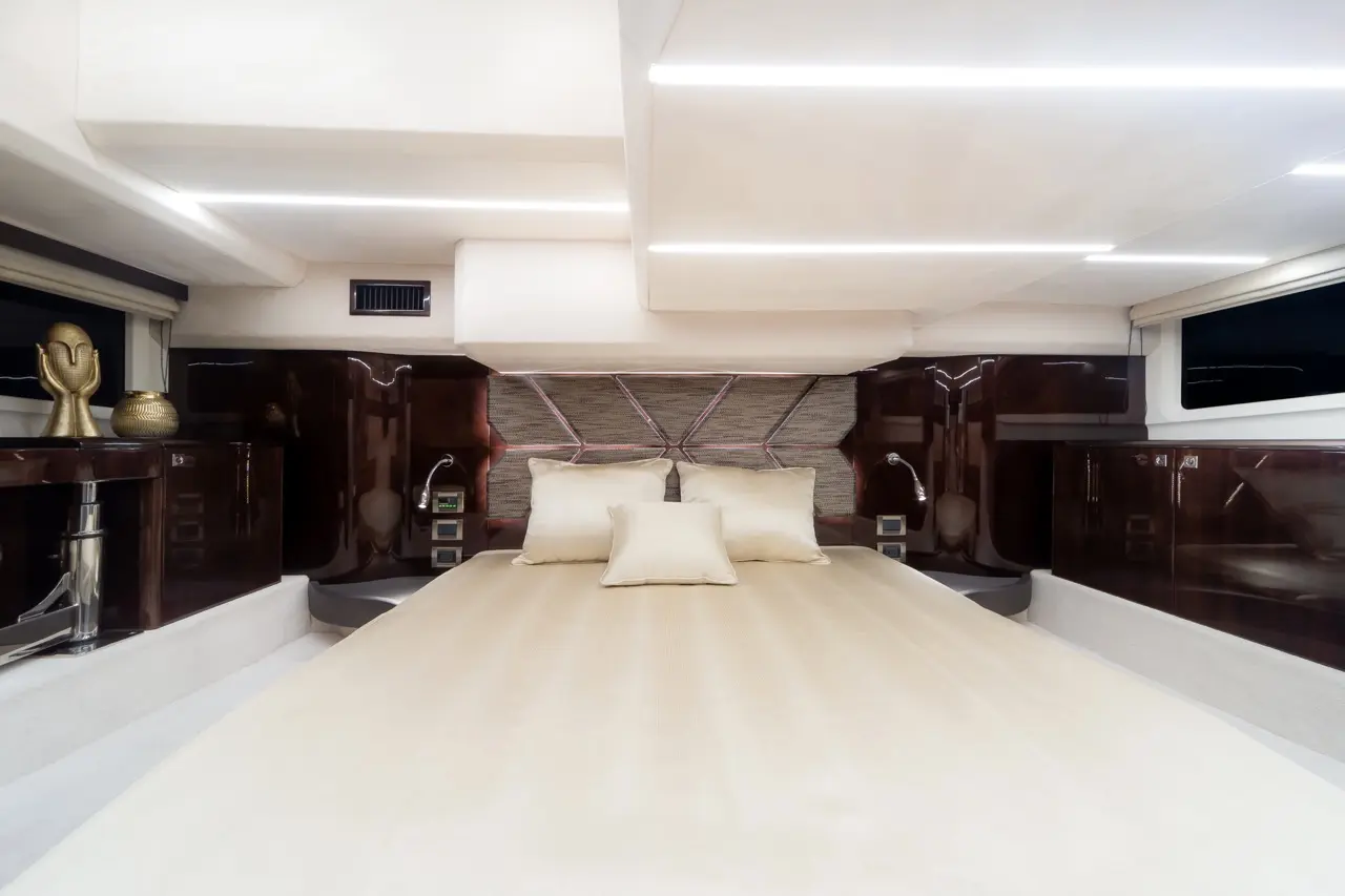 Stylish yacht bedroom featuring a large bed with neutral bedding, decorative pillows, modern lighting, and elegant wooden details.