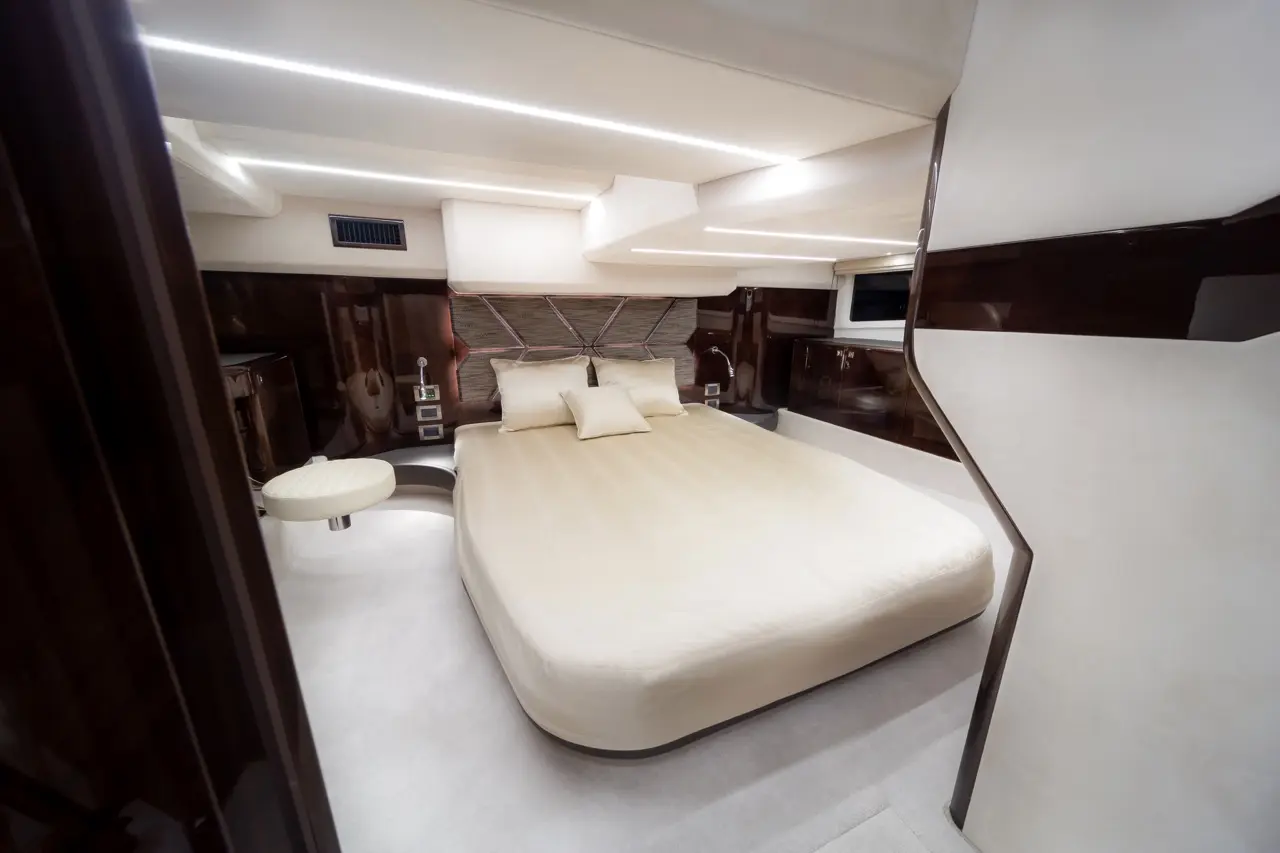 Luxurious yacht cabin featuring a large cream bed, plush pillows, stylish lighting, and modern furniture.