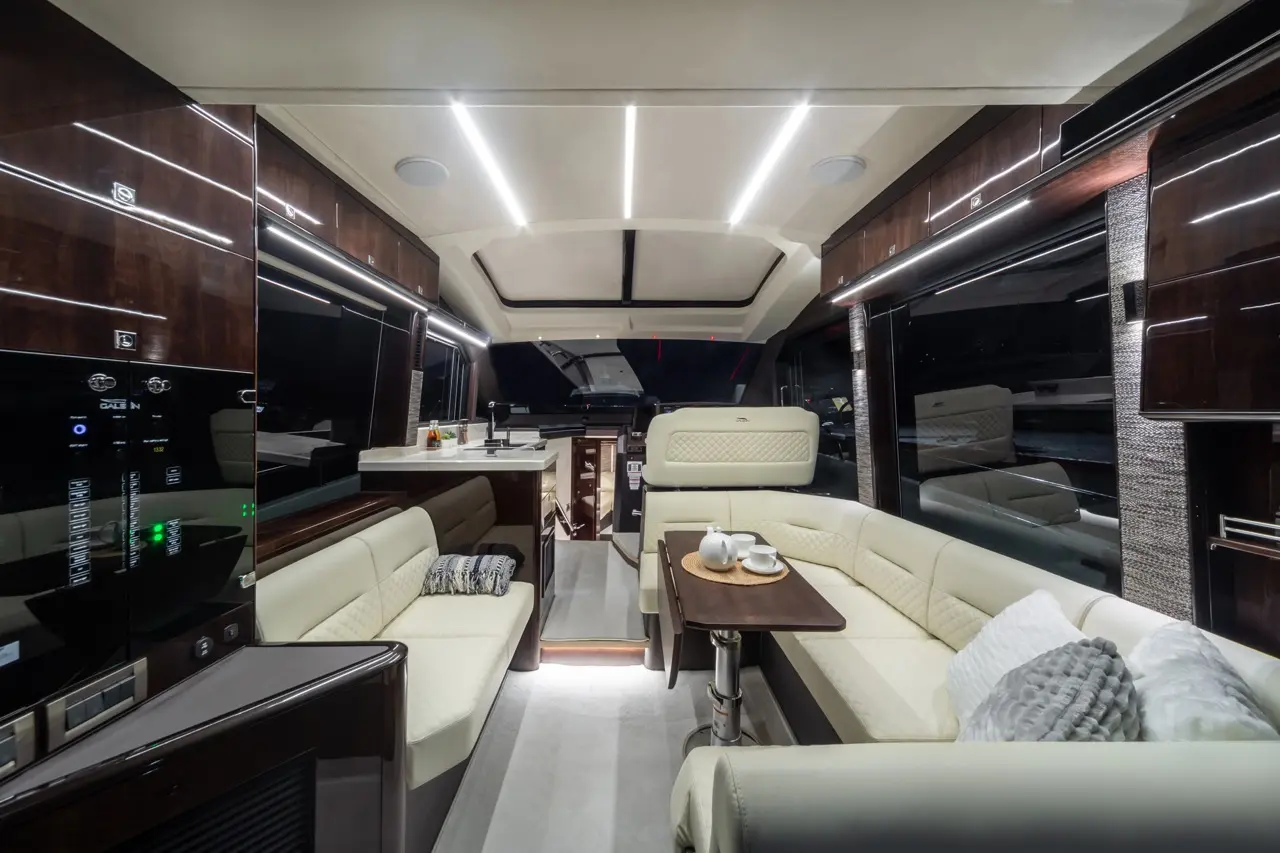 Modern yacht interior with plush seating, a coffee table, and a kitchen area, illuminated by sleek LED lights.