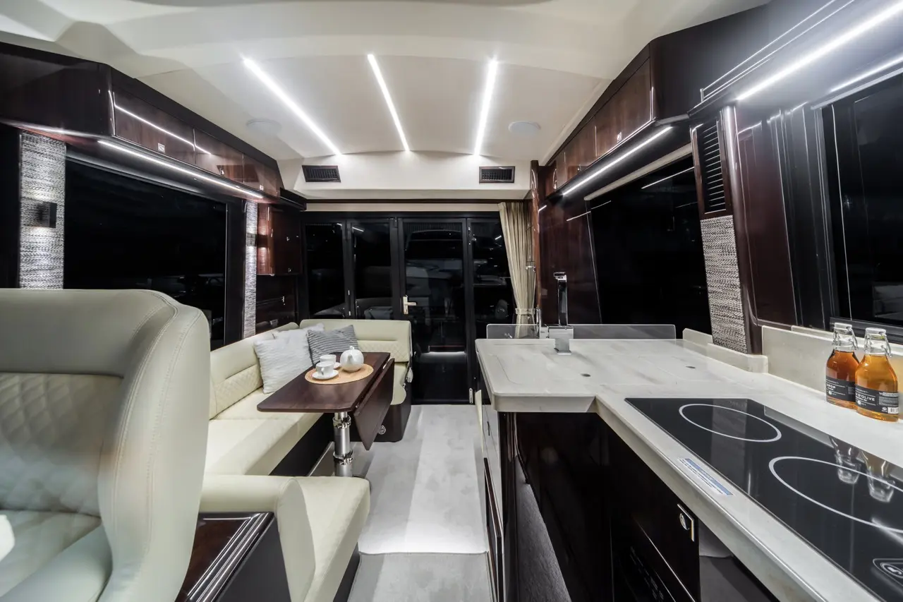 Luxurious camper interior featuring a kitchenette, seating area, and large windows, with a modern aesthetic and warm lighting.
