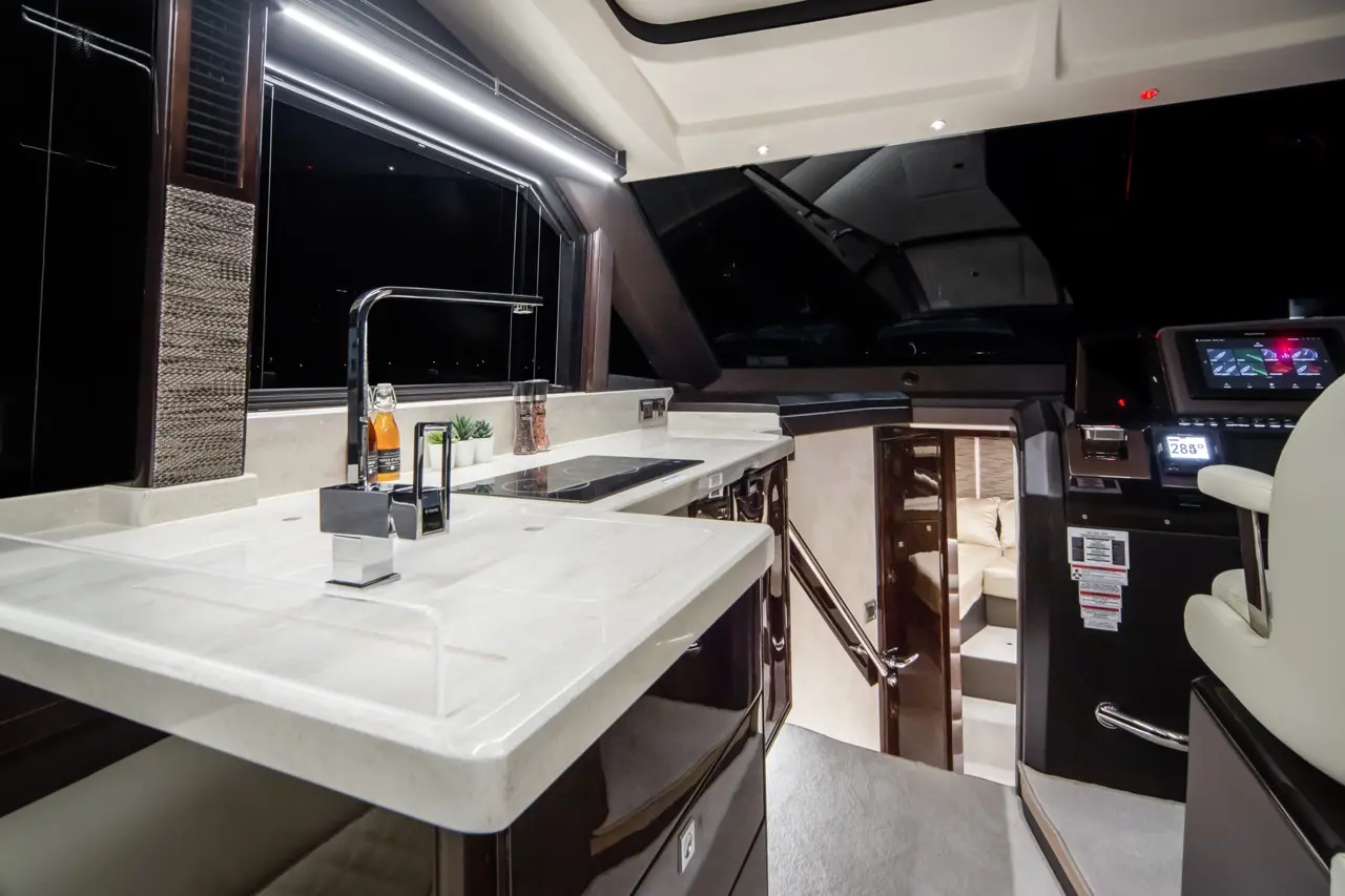 Modern yacht kitchen with sleek white countertop, chrome fixtures, and ambient lighting, featuring a view of the dark night sky.