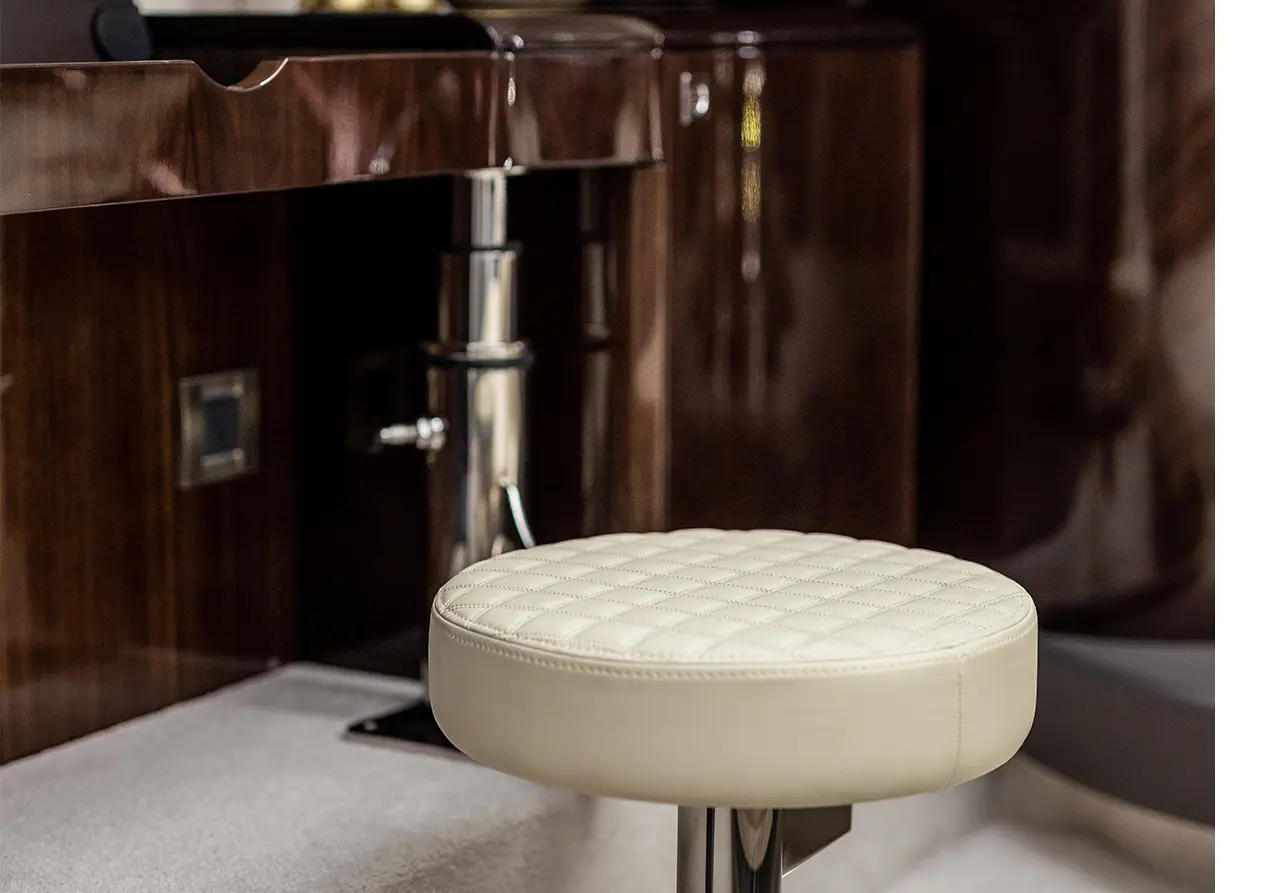 A cushioned cream bar stool with a quilted design, positioned near a sleek wooden counter in an elegant interior space.