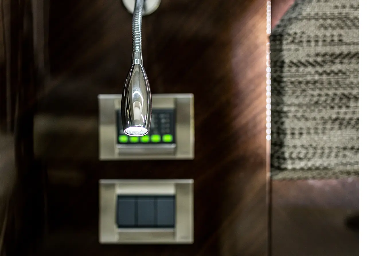 A chrome reading light hangs above a control panel with illuminated buttons and a textured wall surface in the background.