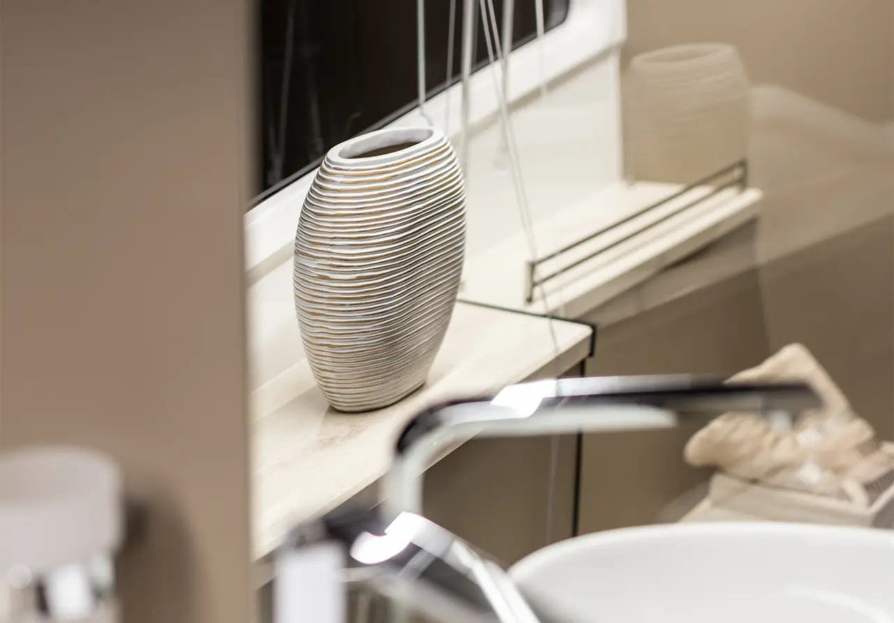 A decorative striped vase on a bathroom countertop, with soft lighting and a blurred sink in the foreground.